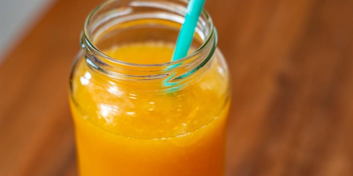 Close-up of fresh orange juice in a mason jar with teal straw on wooden table.