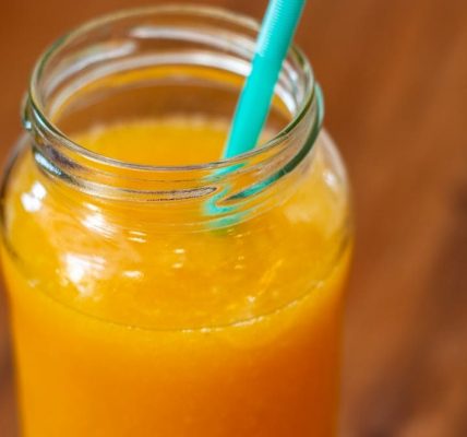 Close-up of fresh orange juice in a mason jar with teal straw on wooden table.