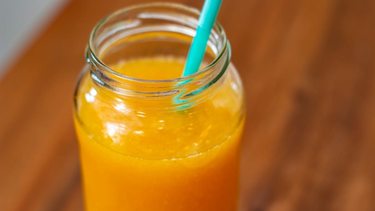 Close-up of fresh orange juice in a mason jar with teal straw on wooden table.
