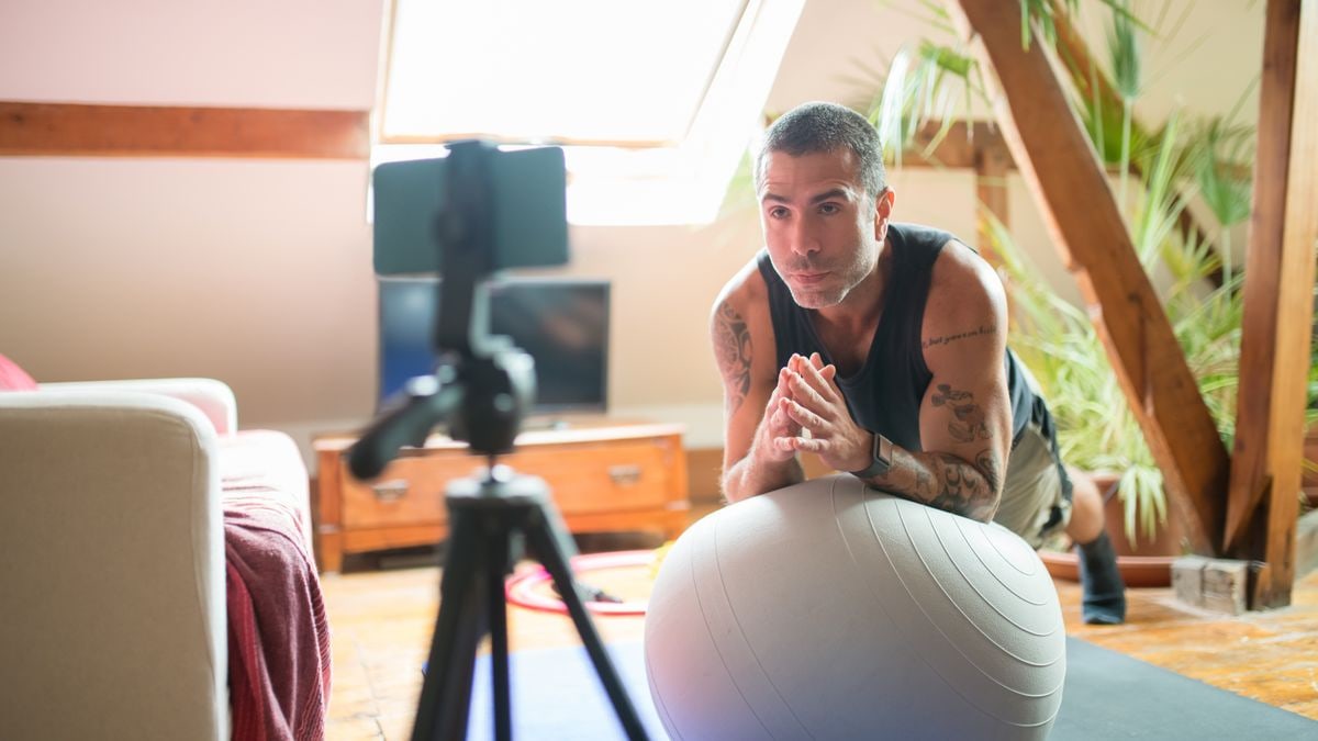 A man works out with a stability ball in a cozy home gym, recorded on a smartphone.