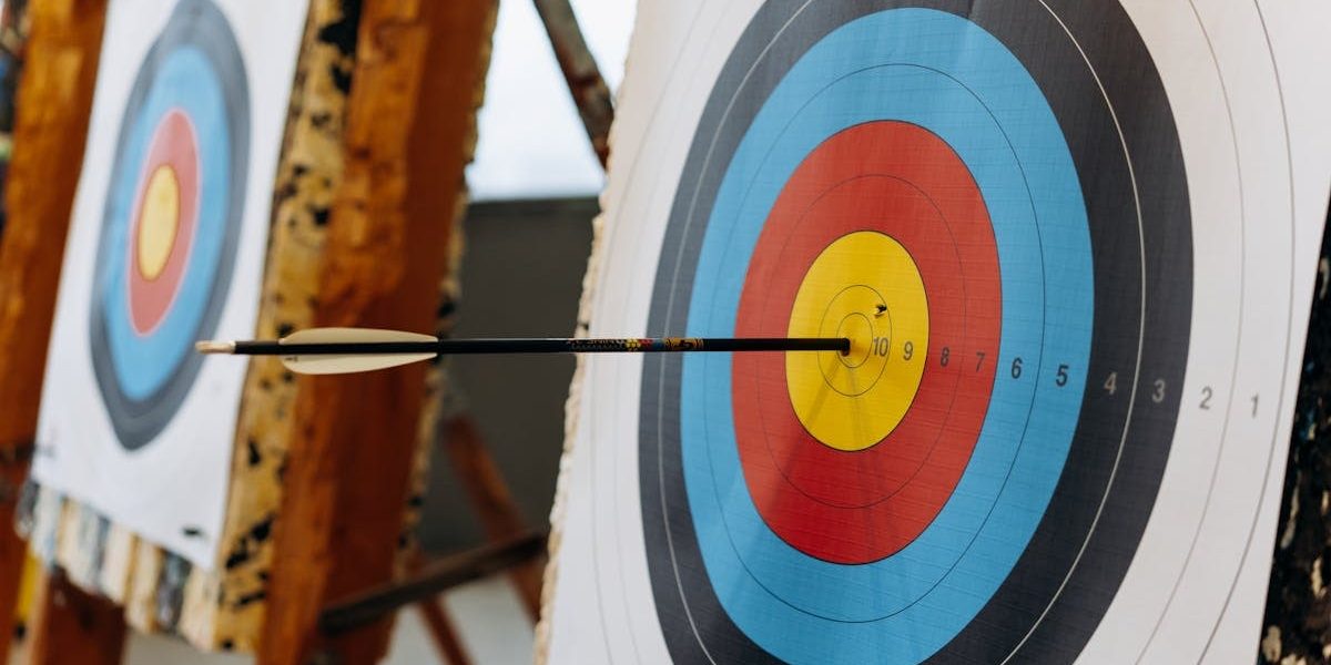 An arrow hits the bullseye on a colorful target in an indoor archery range.