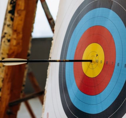 An arrow hits the bullseye on a colorful target in an indoor archery range.