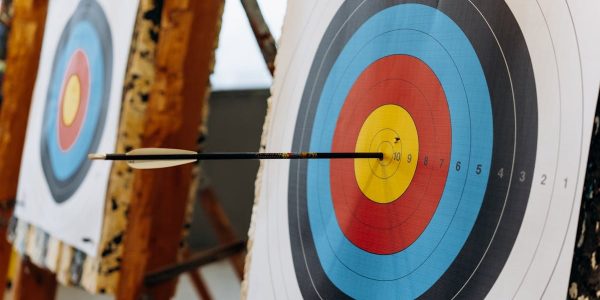 An arrow hits the bullseye on a colorful target in an indoor archery range.